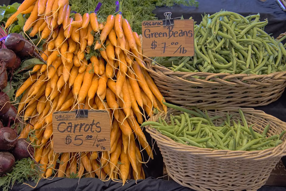 A display of fresh organic carrots and green beans at a local market stall.